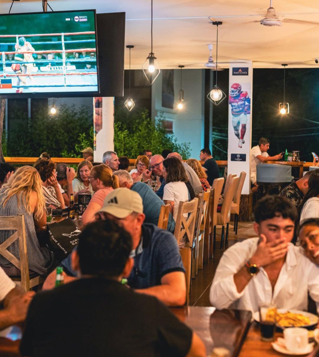 Clientes disfrutando del ambiente deportivo mientras ven boxeo en las pantallas